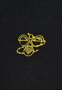 Svart tyg med en gul broderad design av ett stiliserat bi med intrikata linjer och former, inklusive cirkulära och triangulära element.