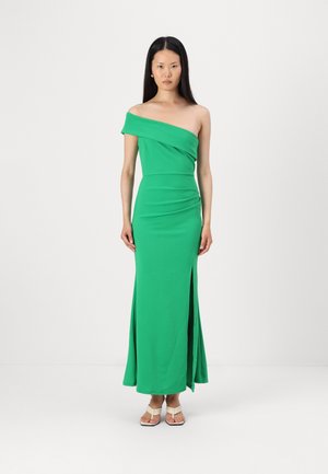Green, one-shoulder dress made of smooth fabric. Fitted silhouette with a side slit. Model wears flat sandals with a minimal design.