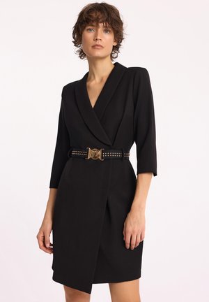 Czarna sukienka kopertowa z głębokim dekoltem w kształcie V, z rękawami o długości trzy czwarte i dopasowaną talią. Akcentowana złotym paskiem z klamrą oraz detalami w ćwieki.