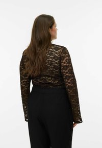 Melns mežģīņu tops ar garām piedurknēm, ziedu rakstiem, caurspīdīgu materiālu un piegulošu dizainu, kombinēts ar vaļīgām melnām biksēm.