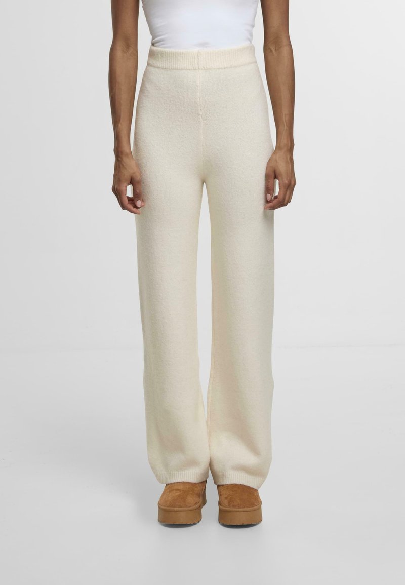 Miękkie, kremowe spodnie w stylu szerokich nogawek z żebrowanym pasem; wykonane z fakturowanej tkaniny. W połączeniu z brązowymi platformami z zamszu.