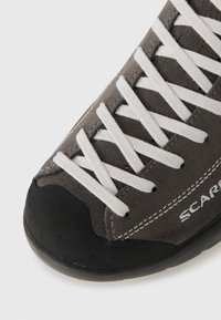 Szare zamszowe buty wspinaczkowe z białymi sznurówkami, gumowym czubkiem i kontrastującym przeszyciem. Zaprojektowane z myślą o trwałości i trakcji.
