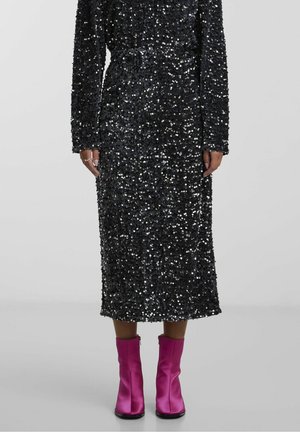 Schwarzes Paillettenkleid mit langen Ärmeln, Gürtel-Detail und mittlerer Länge, kombiniert mit rosa Satin-Knöchelstiefeln mit Reißverschluss.