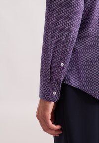 Camicia a maniche lunghe in tessuto viola scuro con un piccolo motivo circolare in rosa e bianco. Presenta polsini button-down bianchi e un orlo curvo.
