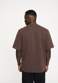 Brun bomulds t-shirt med korte ærmer, rund halsudskæring, afslappet pasform og minimal syning på kanten og ærmerne.