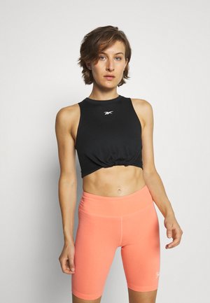 Top corto senza maniche nero con fronte annodato e logo bianco, abbinato a pantaloni ciclistici color corallo. Tessuto liscio con design aderente.
