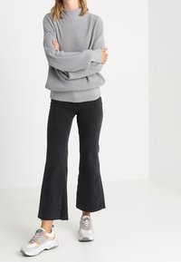 Pull gris côtelé surdimensionné à col montant, associé à un jean noir évasé et des baskets multicolores. Tissu texturé et design décontracté.