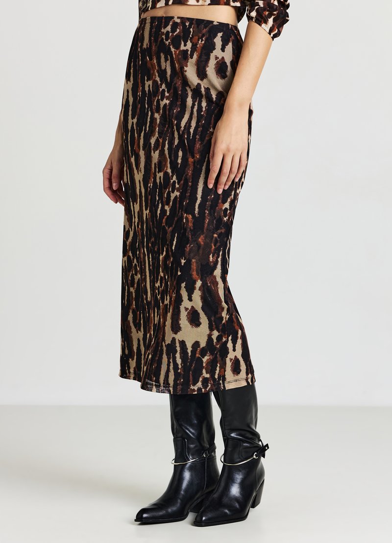 Eine Frau trägt einen Midirock mit Leopardenmuster, kombiniert mit schwarzen Stiefeln mit Absatz, die metallische Kettendetails aufweisen.