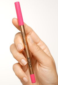 Matita per labbra oro e rosa tenuta tra le dita. Presenta un cappuccio rosa e un audace marchio "KIKO MILANO" sul corpo. Texture liscia.