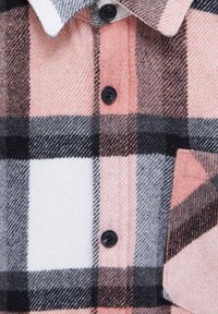 Gros plan d'un tissu à carreaux rose, blanc, noir et gris avec trois boutons noirs et une poche cousue sur une chemise à col.