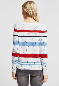 Striped sweater in white, featuring red, blue, and black horizontal stripes with small anchor patterns throughout. Soft knit fabric.