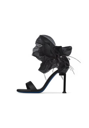 Sandalo nero con tacco alto sottile a stiletto, cinturino singolo per le dita e grande fiore decorativo in tessuto nero con piume sul cinturino alla caviglia.