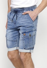 Denim shorts med en lys blå vask, elastisk talje med snor, flere lommer og optrukket kant.