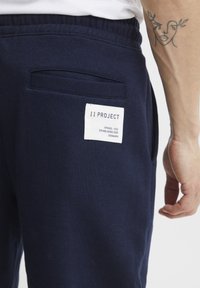 Navy blue sweatpants made of soft fabric featuring a back pocket with a visible white label displaying "11 PROJECT."