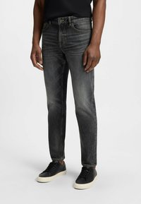 Jeans in denim neri con una finitura sbiadita, taglio dritto e design a cinque tasche, abbinati a sneaker nere con suola bianca.
