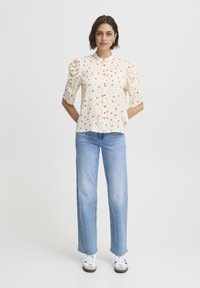 White blouse with red polka dots, featuring short puff sleeves and a high neckline, paired with light blue straight-leg jeans and white sneakers.