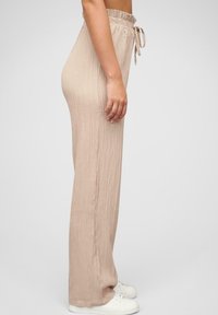 Pantalons beige à large jambe, texturés, avec une taille élastique et un cordon de serrage. Présente un motif légèrement côtelé et une coupe ample.