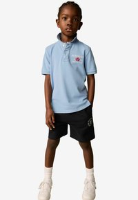 Ljusblå polo med krage och broderad logotyp, i kombination med svarta shorts med grafisk detalj. Vita sneakers och strumpor fulländar outfiten.