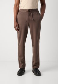 Brune bukser med elastisk talje og justerbar snor, sidelommer og blød tekstur. Tæt design og afslappet stil.