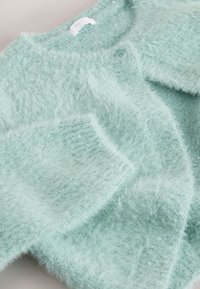 Cardigan en maille duveteuse bleu clair avec poches avant et petites paillettes dispersées sur le tissu.