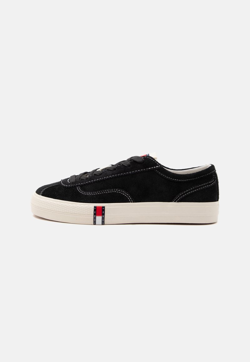 Baskets basses noires en suédine avec semelle blanche, lacets noirs et logo Tommy Jeans rouge, blanc et bleu sur le côté de la semelle.