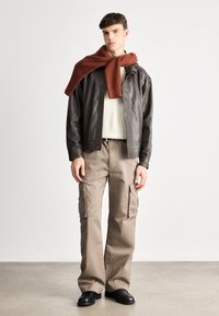 Pruun nahast pommitaja jakk kreemja sviitriga, beežid cargo-püksid küljetaskutega ja roostetähtede ribatud sall. Mustad kingad.