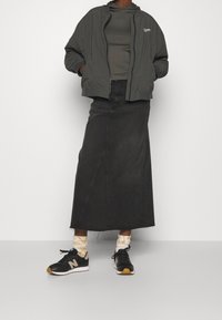 Gonna lunga in denim nera, giacca bomber grigia con zip, t-shirt grigia, sneakers nere con accenti color cioccolato, e calze bianche a fantasia.