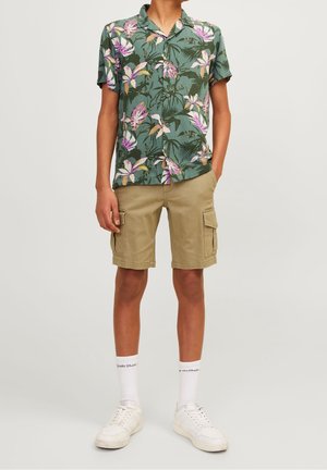 Zielona koszula w kwiaty z krótkim rękawem, z fioletowymi i żółtymi akcentami, zestawiona z beżowymi szortami cargo z bocznymi kieszeniami. Białe trampki i skarpetki.