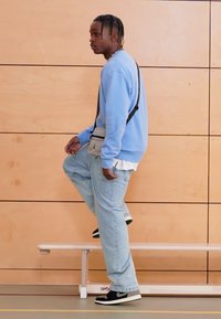 Világoskék pulóver, bővülő szabású farmernadrág és fekete-fehér tornacipő. Kis válltáska és réteges öltözet fehér inggel alatta.