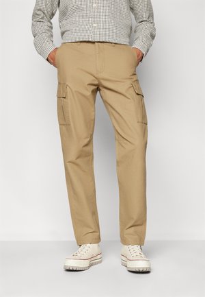Khaki cargo pants featuring two side pockets, straight leg design, and a cotton blend fabric. Paired with white sneakers, no visible patterns.