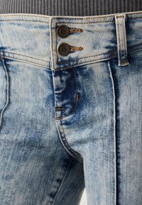 Jean en denim bleu clair avec une taille haute, une fermeture à double bouton, des coutures contrastantes et une subtile texture délavée.