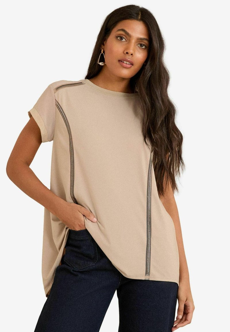Top corto a maniche corte beige chiaro con scollatura a barca, caratterizzato da dettagli di cucitura scura a contrasto lungo i lati e una vestibilità comoda.