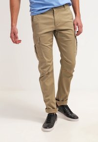 Pantalones cargo caqui con un corte ajustado, hechos de una tela ligera. Cuentan con bolsillos frontales y bolsillos laterales para cargo. Combinados con zapatillas negras.