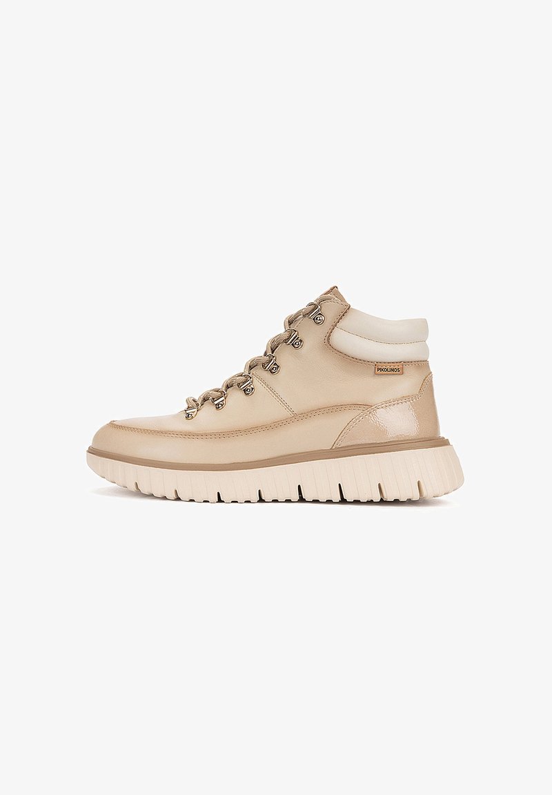 Baskets mi-hautes beige clair avec semelle blanche épaisse, lacets à l'avant avec œillets métalliques, col matelassé et petite étiquette de marque sur le côté.