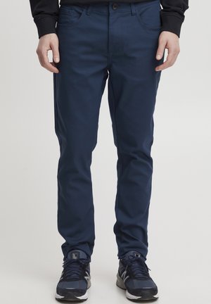 Chinos elásticos de color azul marino con una textura suave, cierre de botón contrastante y diseño de cinco bolsillos. Combinados con zapatillas deportivas negras.