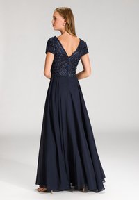 Robe de soirée marine avec un corsage perlé, des manches courtes et un dos en V profond, sa jupe A-line fluide et une texture légère et lisse.