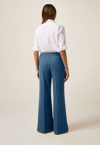 Pantaloni a gamba larga di un azzurro chiaro realizzati in un morbido tessuto fluido; vita elastica e texture liscia; abbinati a una camicia bianca con colletto.