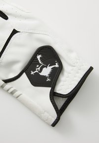 A luva de pele branca apresenta detalhes em preto e um patch texturizado preto com um design gráfico. Inclui detalhes de costura e um formato ajustado.