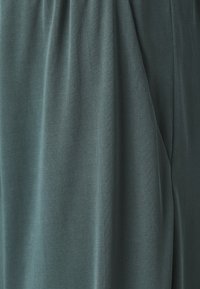 Tissu turquoise avec une texture douce et côtelée, tombant délicatement en plis. Aucun motif ou élément métallique visible.