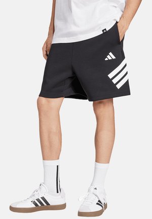 Mann trägt schwarze Adidas-Shorts mit weißem Logo, weiße Adidas-Socken mit schwarzen Streifen und weiße Adidas-Sneaker mit schwarzen Streifen.