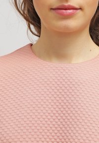 Jasnoróżowa bluzka o fakturze z okrągłym dekoltem, z wzorem w wafel. Prezentuje szczegóły materiału bez innych rozproszeń.