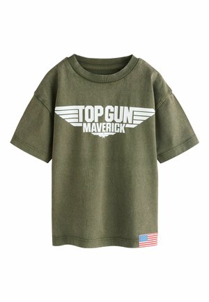Olive green short-sleeve T-shirt with white "TOP GUN MAVERICK" text and wings logo, and a small American flag patch near the hem.