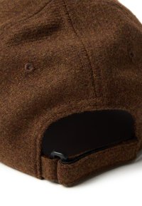 Bruine vilten pet met een gestructureerd oppervlak, gekenmerkt door een ronde vorm, stikdetails en een verstelbare riem aan de achterkant.