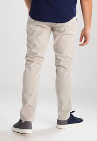 Světle béžové bavlněné kalhoty z twilu, slim-fit střih s viditelnými švy a bočními kapsami, doplněné tmavými botami s kontrastní patou.