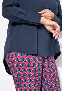 Dunkelblaues Hemd mit Knöpfen und langen Ärmeln, kombiniert mit Leggings in Rot, Blau und Weiß mit geometrischen Mustern.