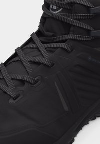 Prim-plan cu bocanc de drumeție negru care prezintă material texturat, șireturi cu model, logo Gore-Tex și talpă robustă pentru utilizare în aer liber.