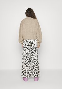 Beige gebreide oversized trui met geribbelde textuur, gecombineerd met brede witte broek met een zwart luipaardprint, en lavendel gekleurde chunky hakken.