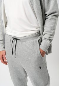 Pantalones de chándal grises en una suave mezcla de algodón, con una cinturilla elástica y un cordón negro, y bolsillos laterales, que muestran un pequeño logo negro.