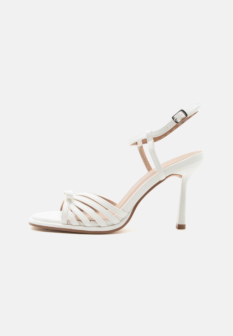 Λευκό πέδιλο με ψηλό τακούνι, λουρί γύρω από τον αστράγαλο και αγκράφα, ανοιχτή μύτη και πολλαπλά στενά λουράκια πάνω από το μπροστινό μέρος του ποδιού.