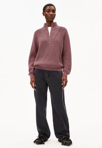 Garen gebreide, geribbelde pullover in mauve met een hoge kraag en halve rits. Gecombineerd met donkere, wijde jeans en zwart fringeschoenen.